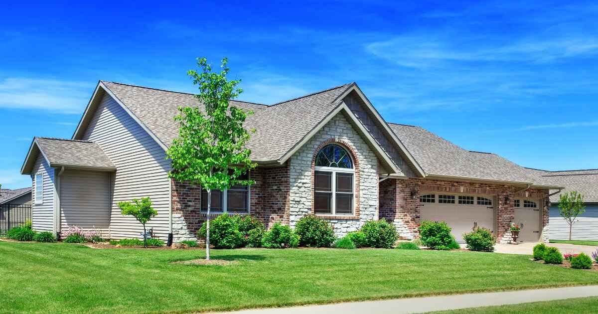 A charming single-story home with a mix of brick and vinyl siding, surrounded by a lush green lawn and a bright blue sky.